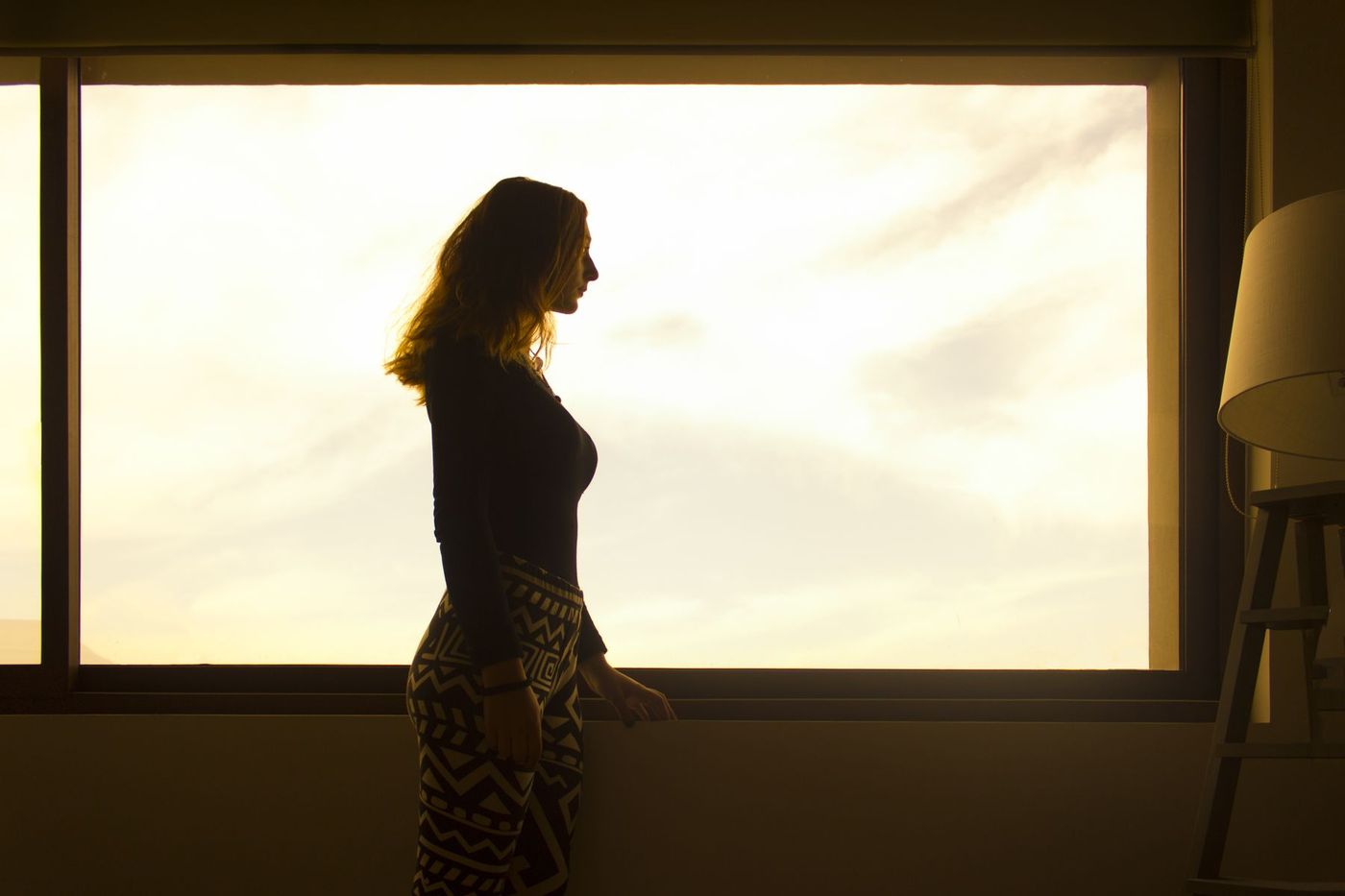 Silhouette d'une personne debout à une fenêtre, dans la lumière de fin de journée