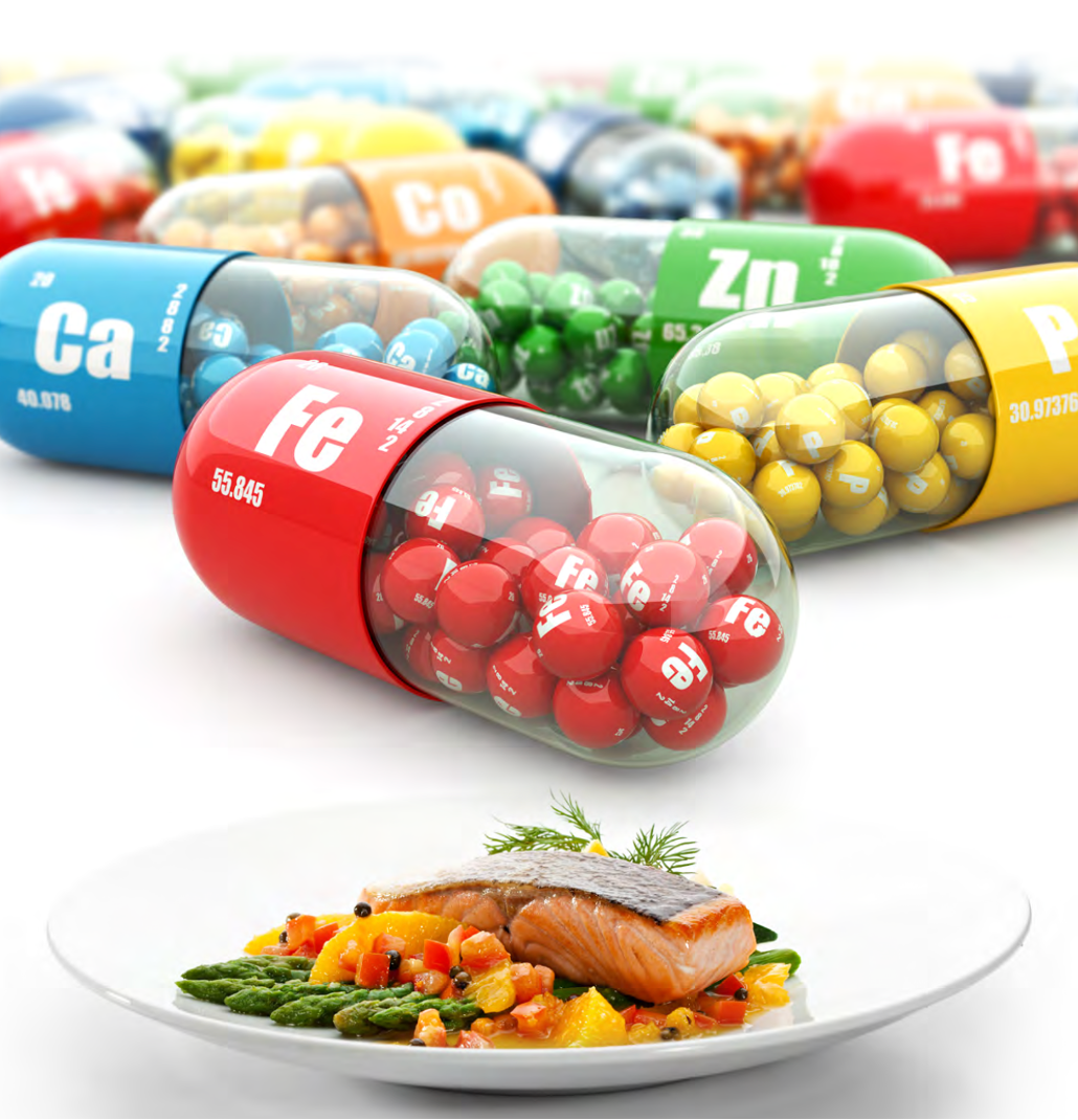 Gélules symbolisant le calcium, le fer, le zinc et le phosphore, devant une assiette de saumon et de légumes